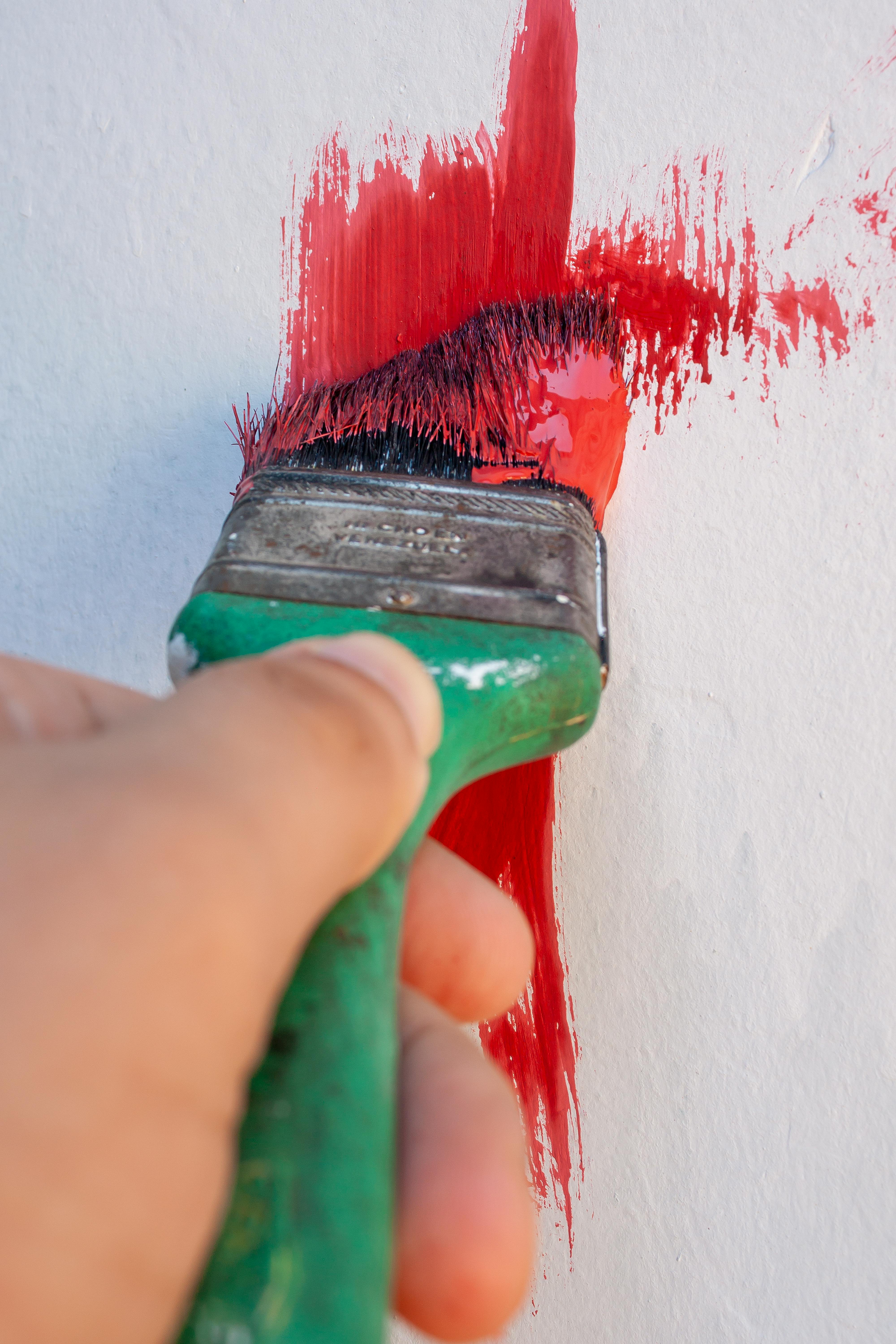 Primo piano di pennello che stende vernice rossa su parete