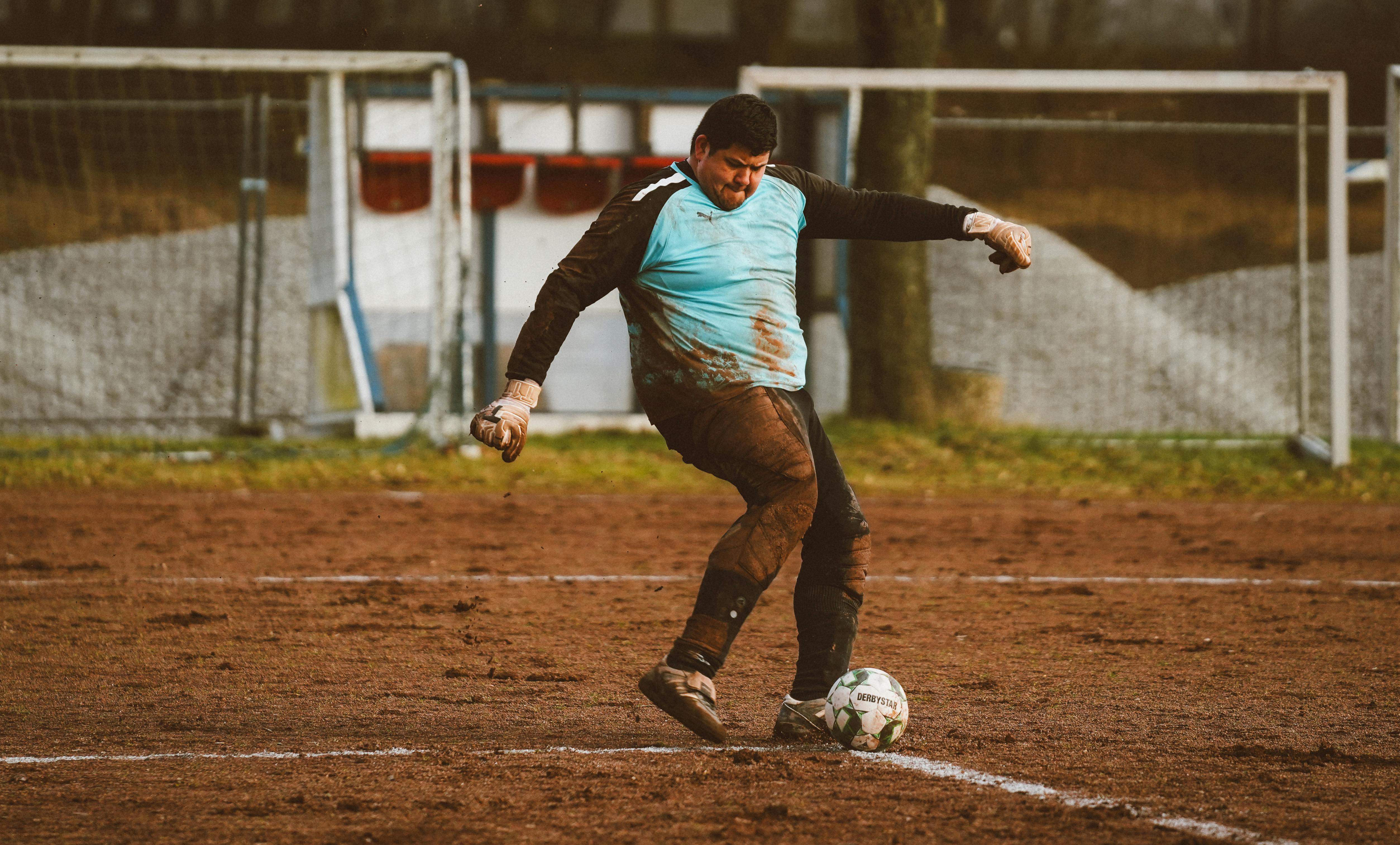 Goalkeeper making a kick on a muddy soccer field, showcasing determination and sport.