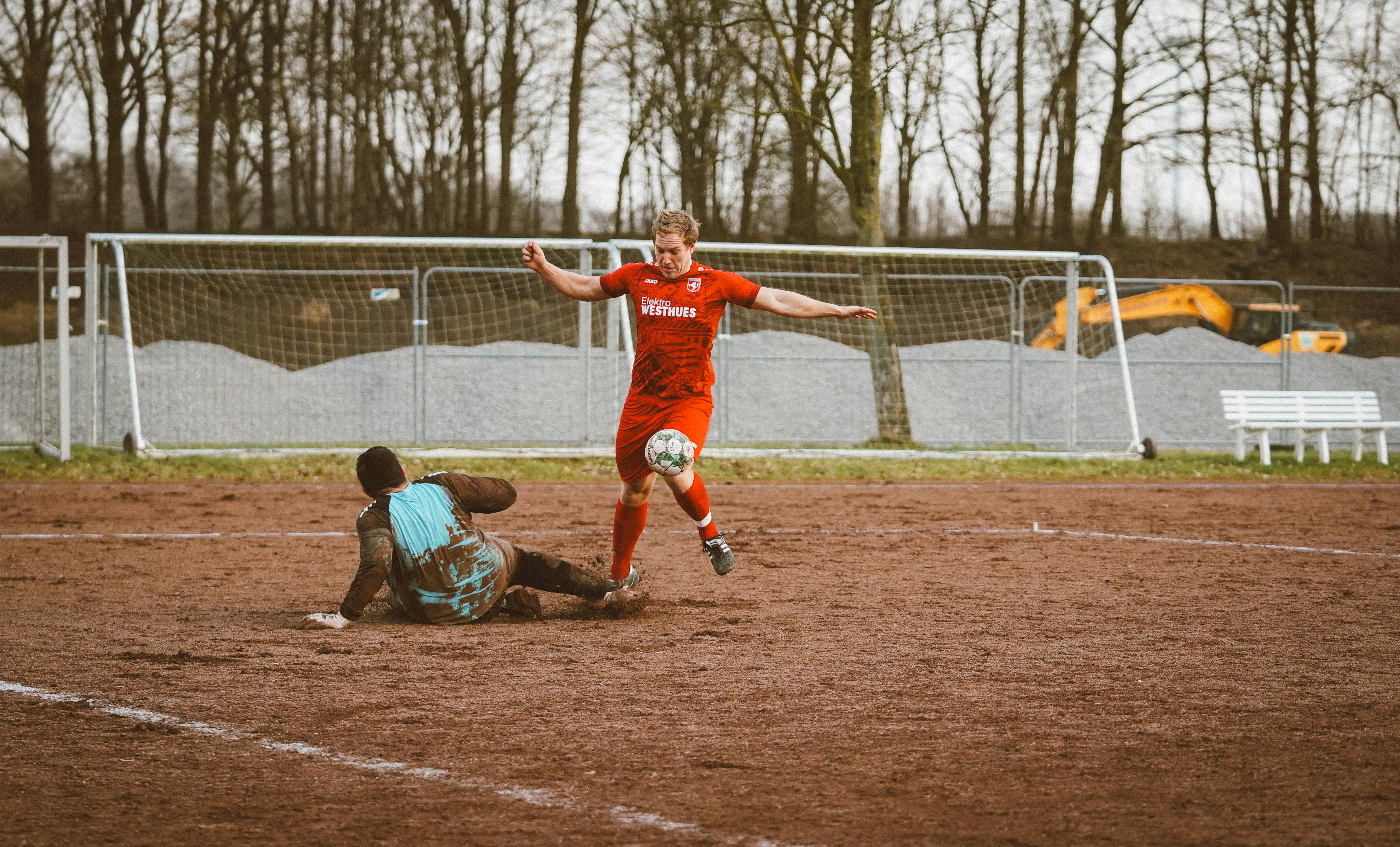 Two players compete fiercely in a soccer match on a muddy field.