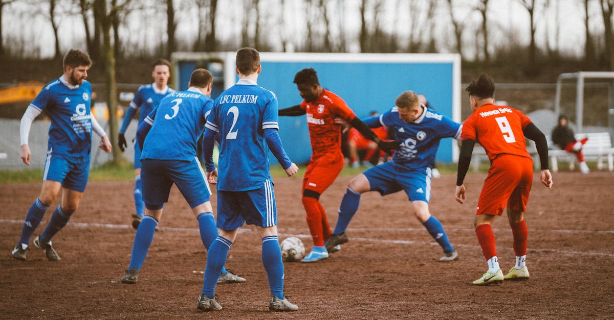 Intense amateur soccer match between blue and red team on a muddy field.