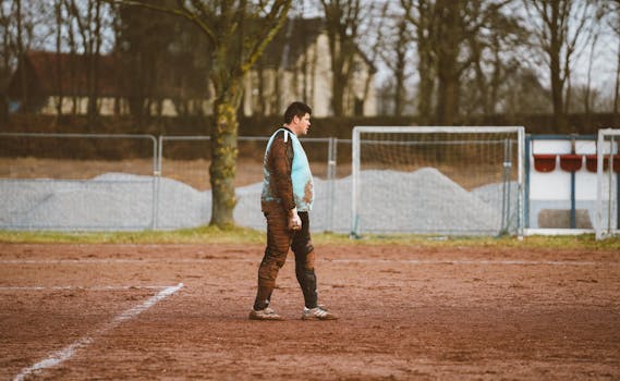 A soccer player stands on a muddy field during training. Outdoors, daytime setting.