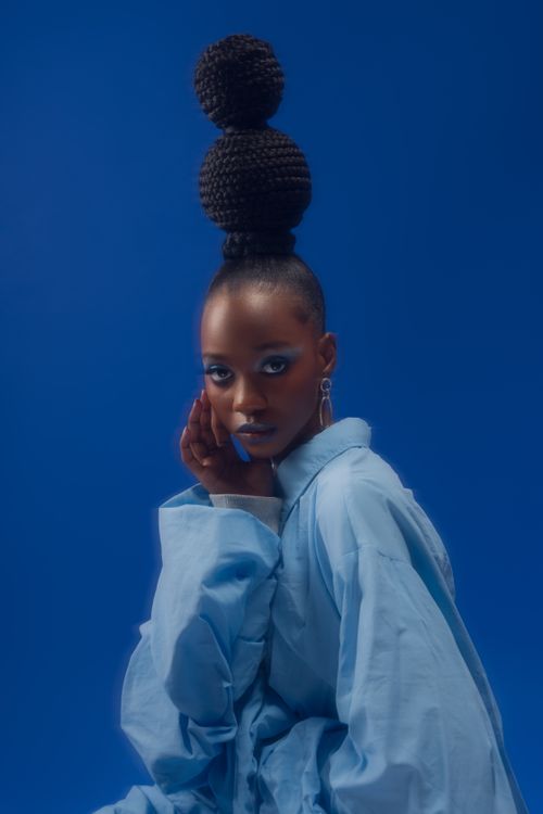 Free Portrait of a woman in artistic pose, wearing a stylish blue outfit against a blue background. Stock Photo