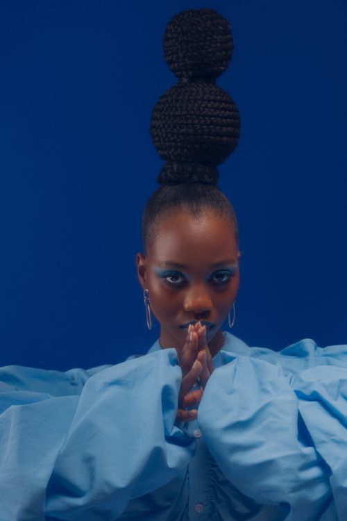 Free Elegant portrait of a woman with unique hairstyle against a blue backdrop, exuding modern style. Stock Photo