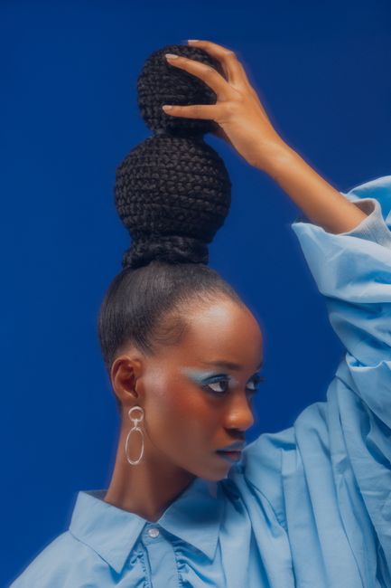 Portrait of a stylish woman with intricate bun hairstyle and statement earrings on a blue background.