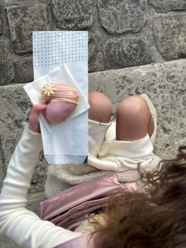 Overhead view of a woman holding a pink frosted pastry on a cobblestone street.