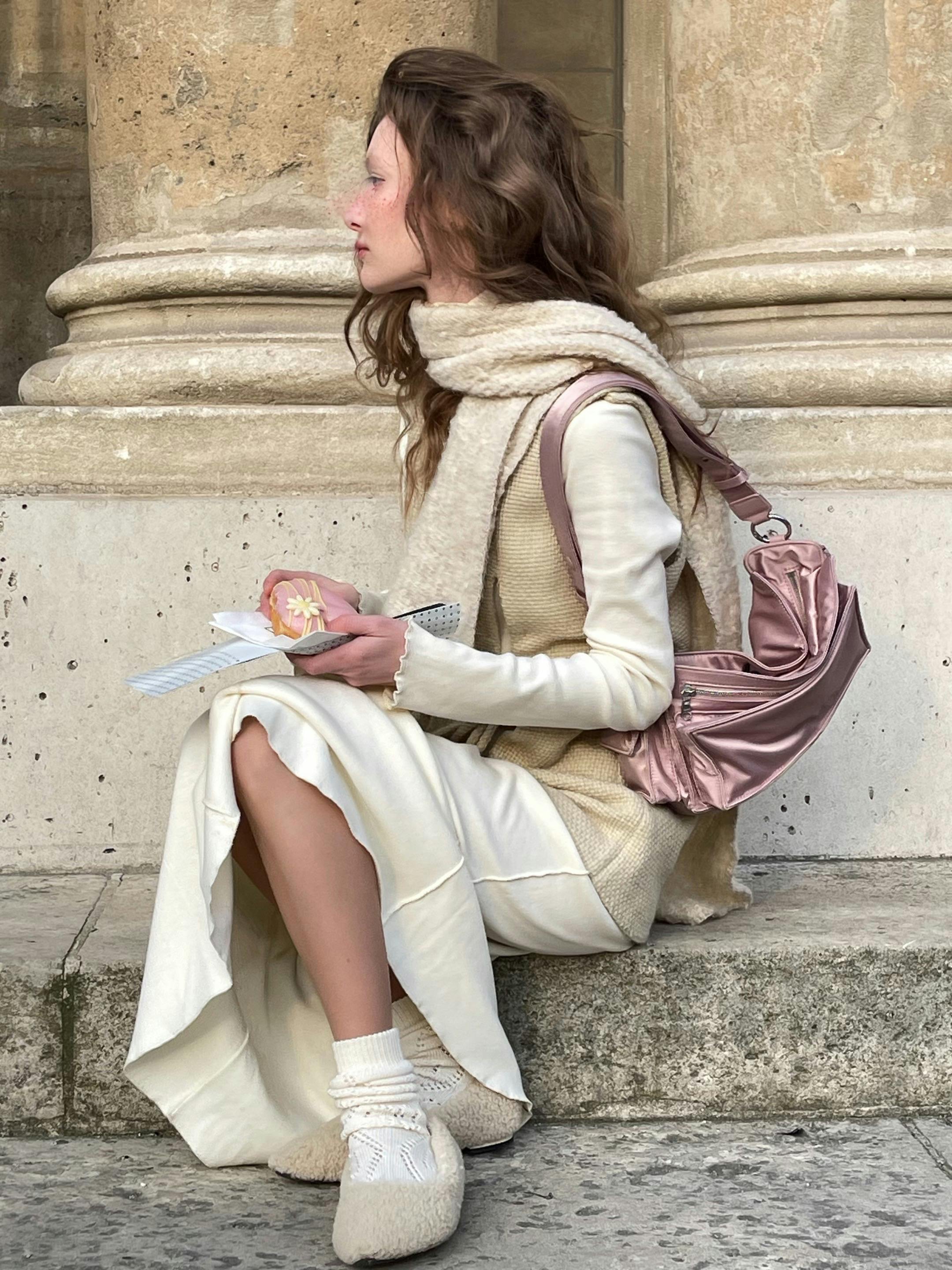 Stylish woman in fall fashion sitting outdoors with book and bag.