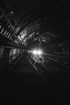 Monochrome view of an approaching train in a dark, moody tunnel setting.