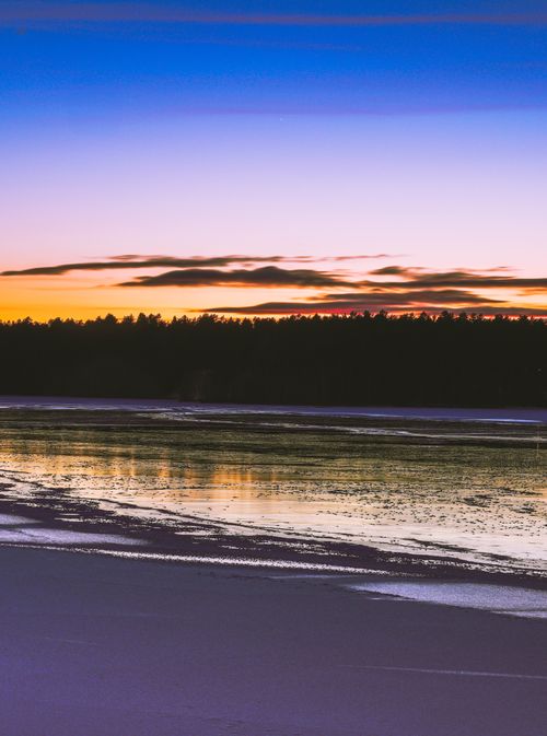 Free A tranquil sunset scene with a calm lake reflecting the vibrant sky above. Stock Photo