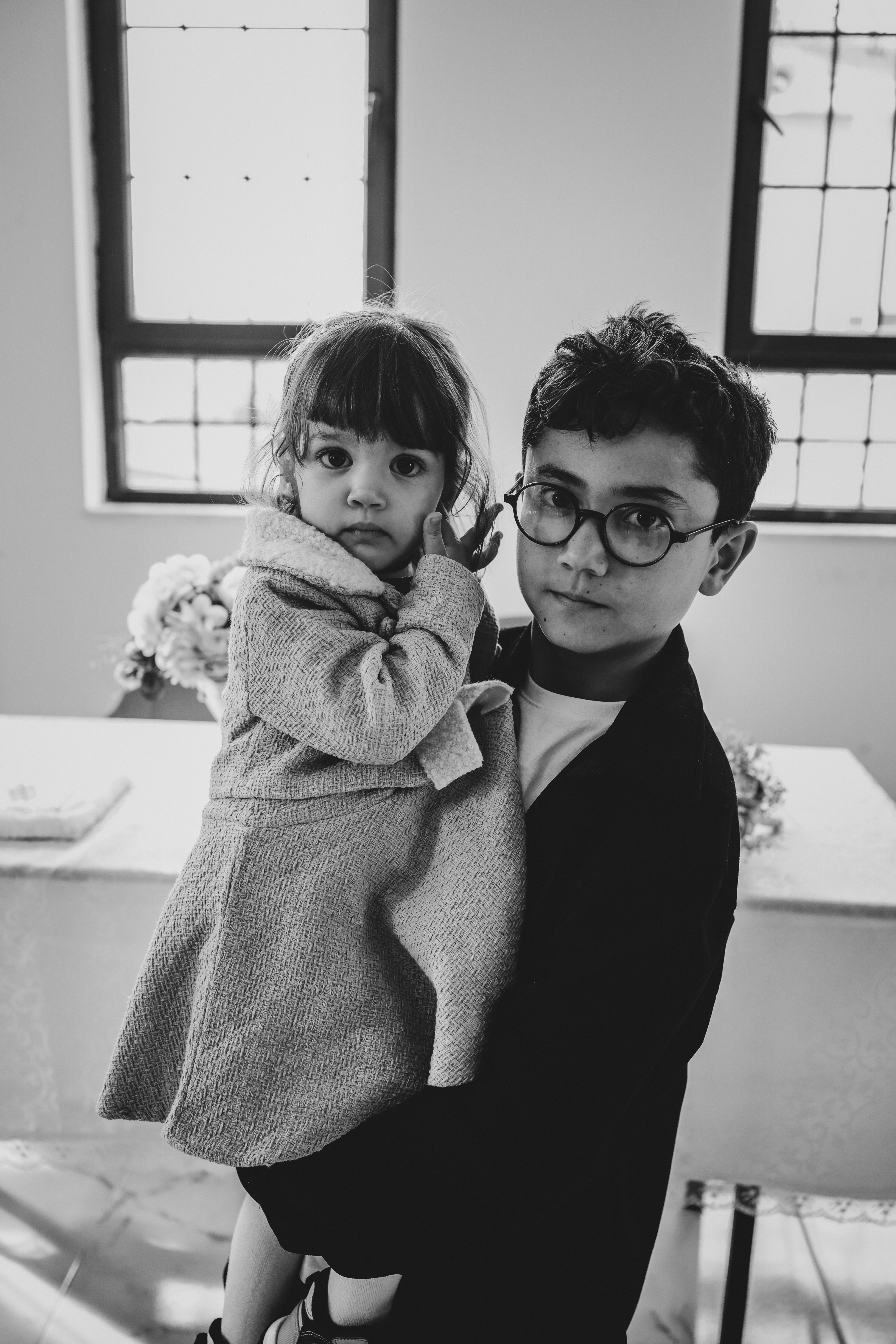 Fotomural Un cautivador retrato en blanco y negro de un niño pequeño sosteniendo a su hermana en el interior, capturando un tierno momento familiar.