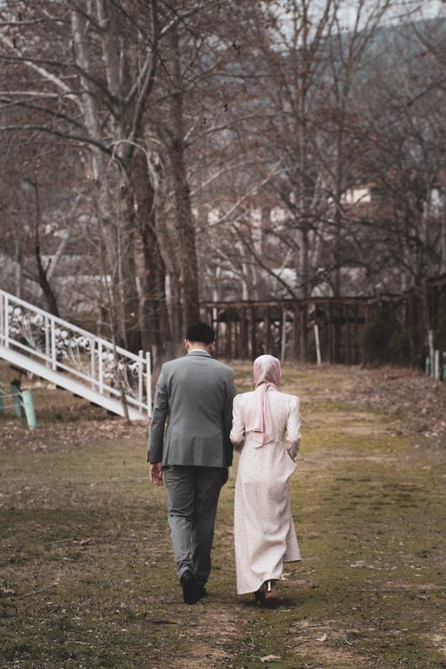 Free A couple walks down a rustic path surrounded by autumn trees, exuding a sense of peace and companionship. Stock Photo