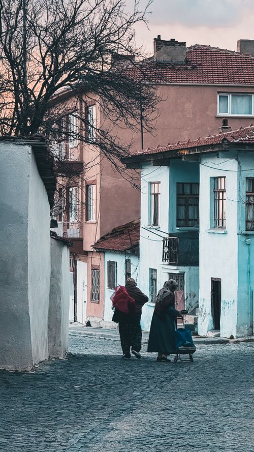 Free A serene street scene with two adults and a child strolling through an old town alley at dusk. Stock Photo
