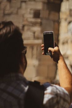 A man capturing a photo of stone architecture with a smartphone.