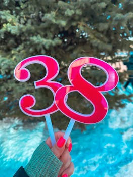 Close-up of a hand holding bright pink number 38 sticks outdoors with snow and trees.