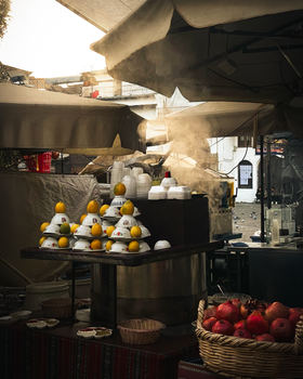 Vibrant outdoor market with stacked tajines and fresh fruits under a canopy.