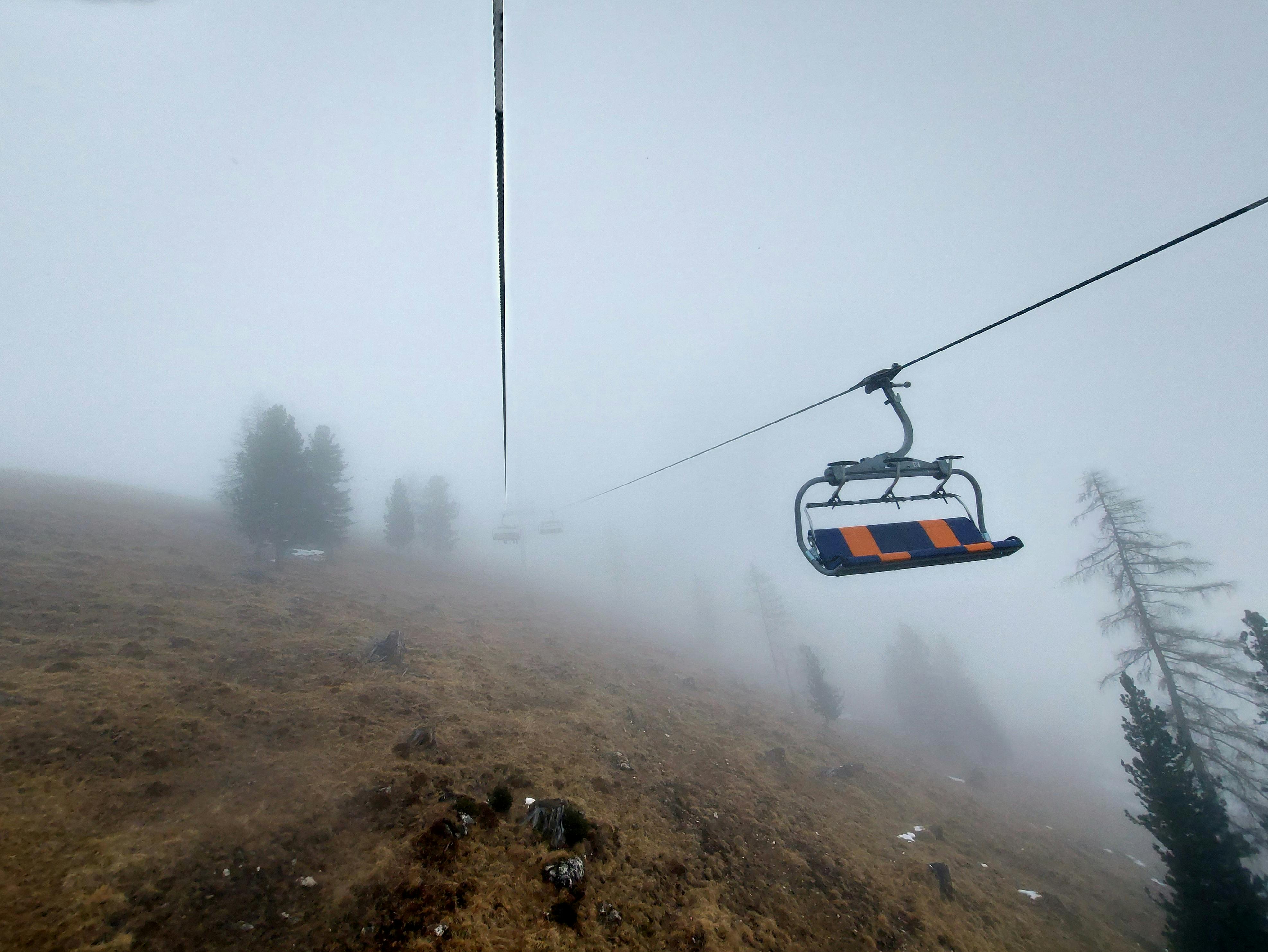 A ski lift ascending a foggy mountain, surrounded by mist and sparse trees, creating a serene adventure scene.