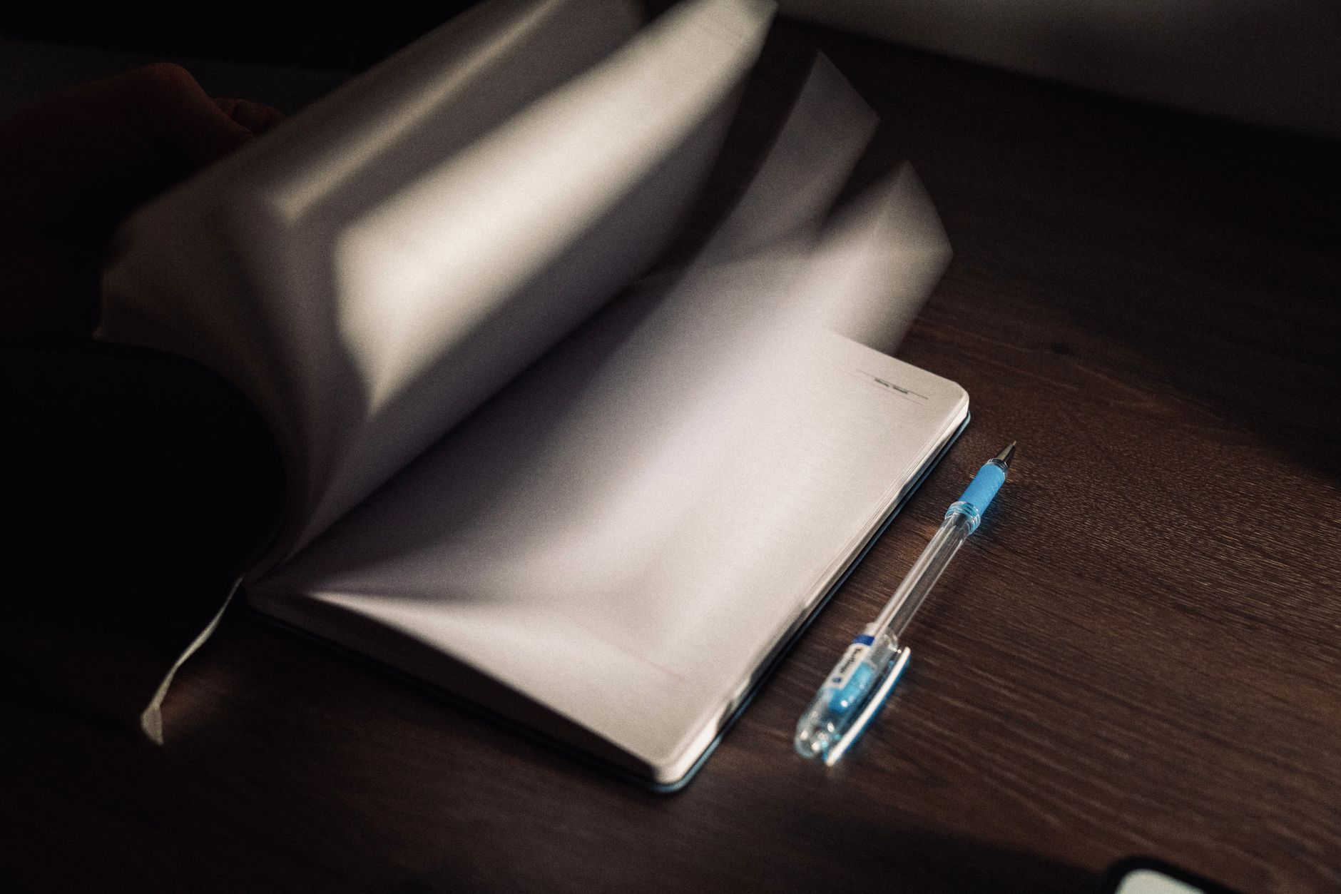 A notebook with turning pages and a pen on a wooden desk in low light.