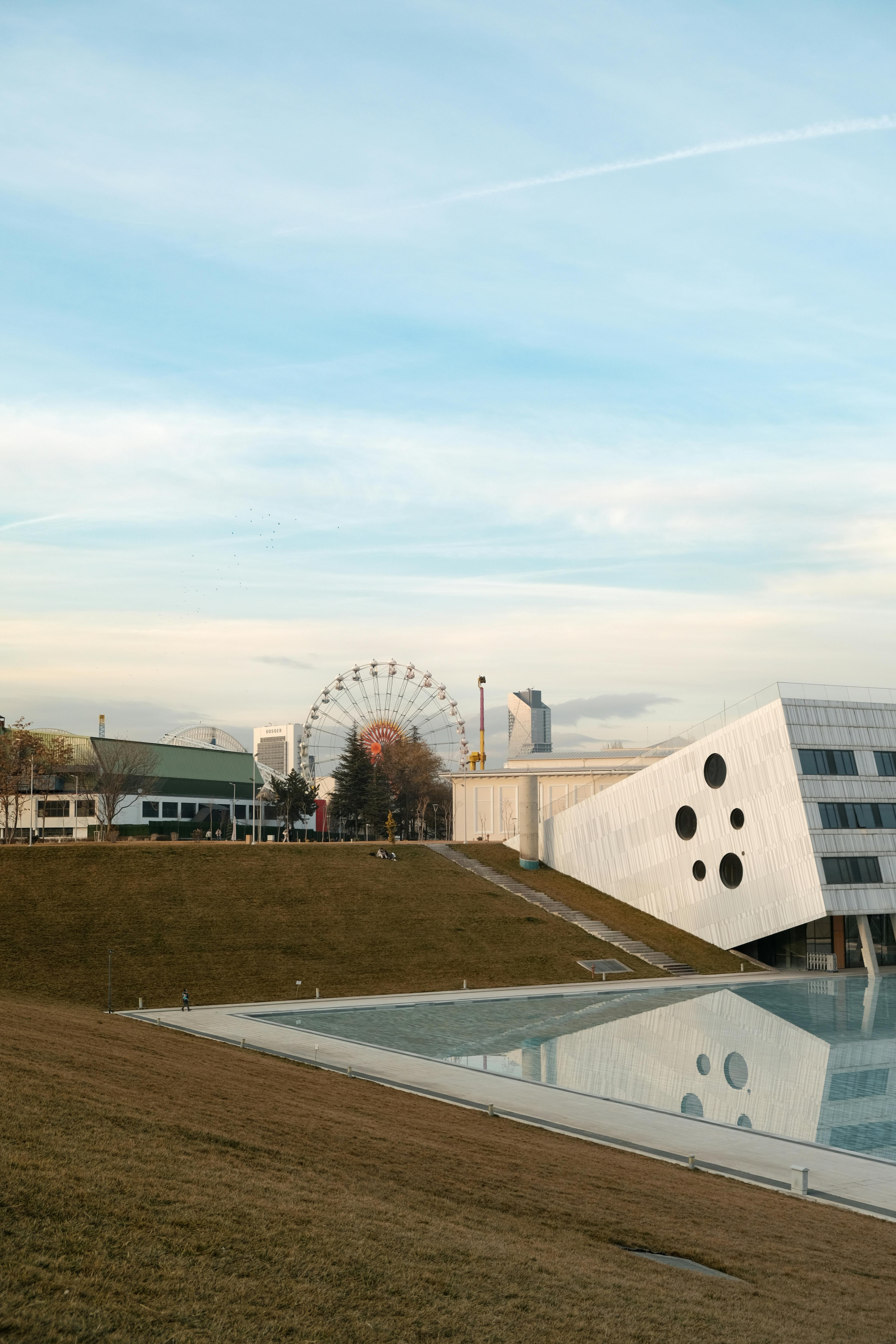 Contemporary buildings and a Ferris wheel in an urban park with clear skies.