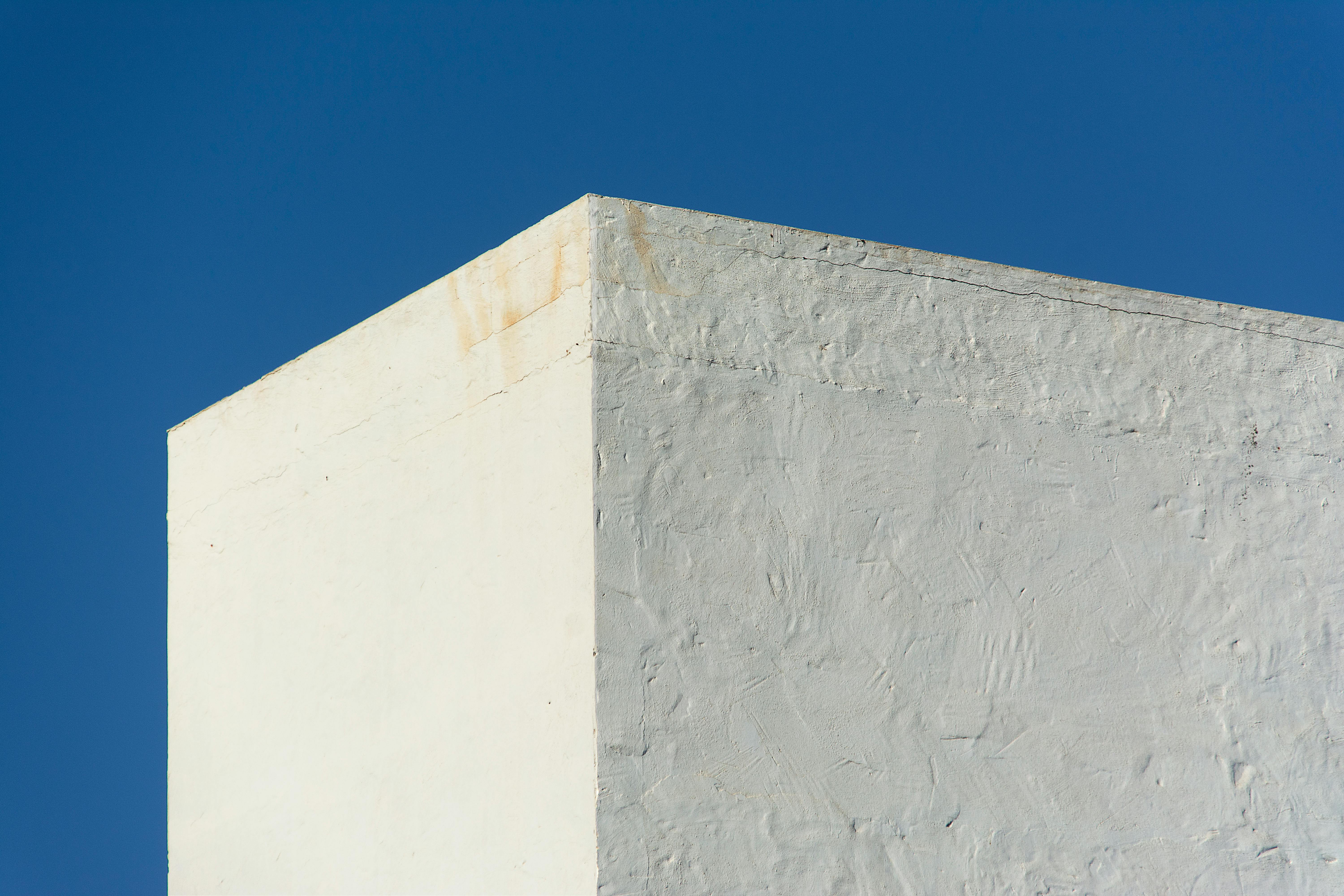 Gratuit Vue abstraite d'un mur blanc texturé contrastant avec un ciel bleu clair, mettant en valeur le minimalisme. Photos