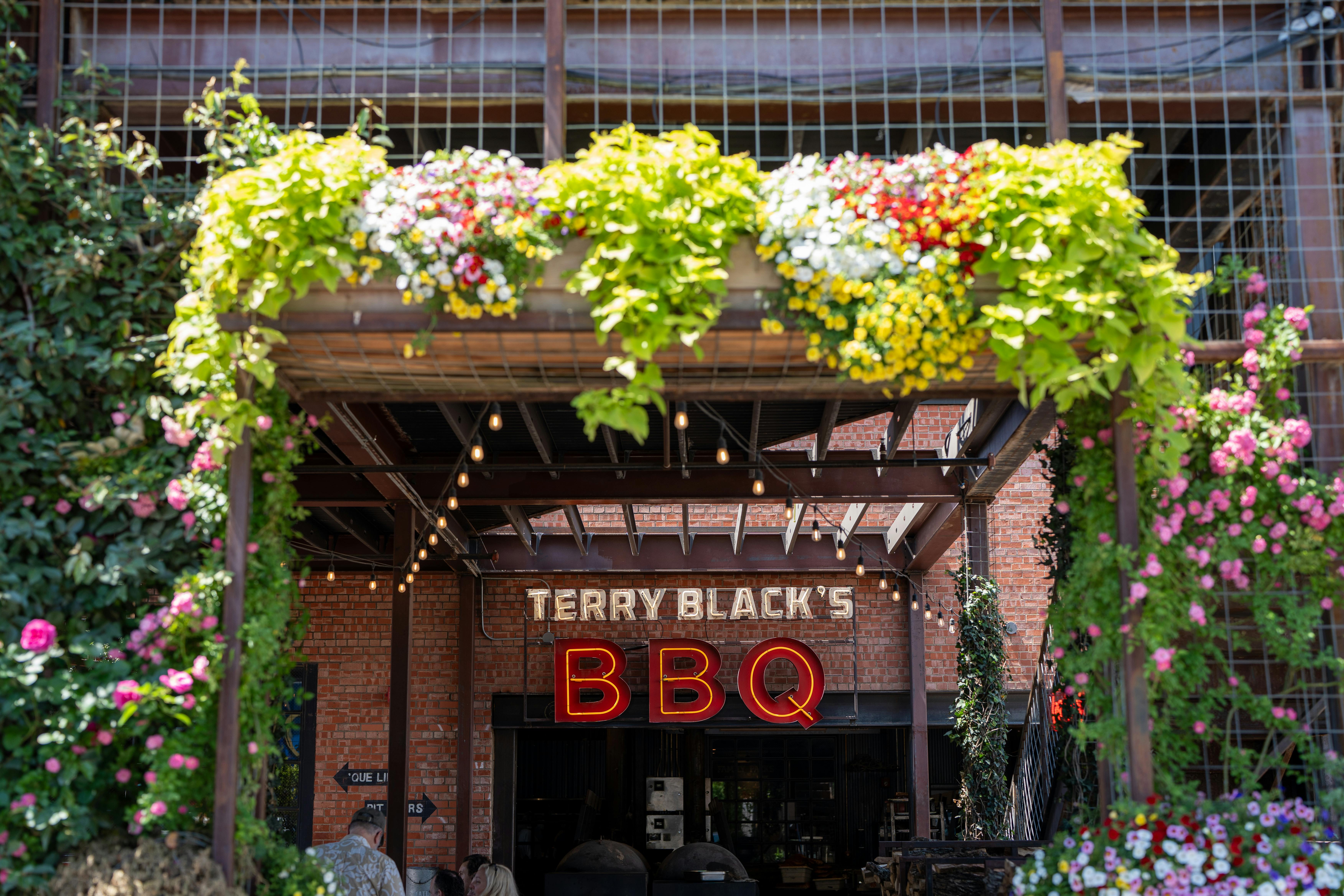 Entrance of Terry Black's BBQ with vibrant flowers in Dallas, Texas.