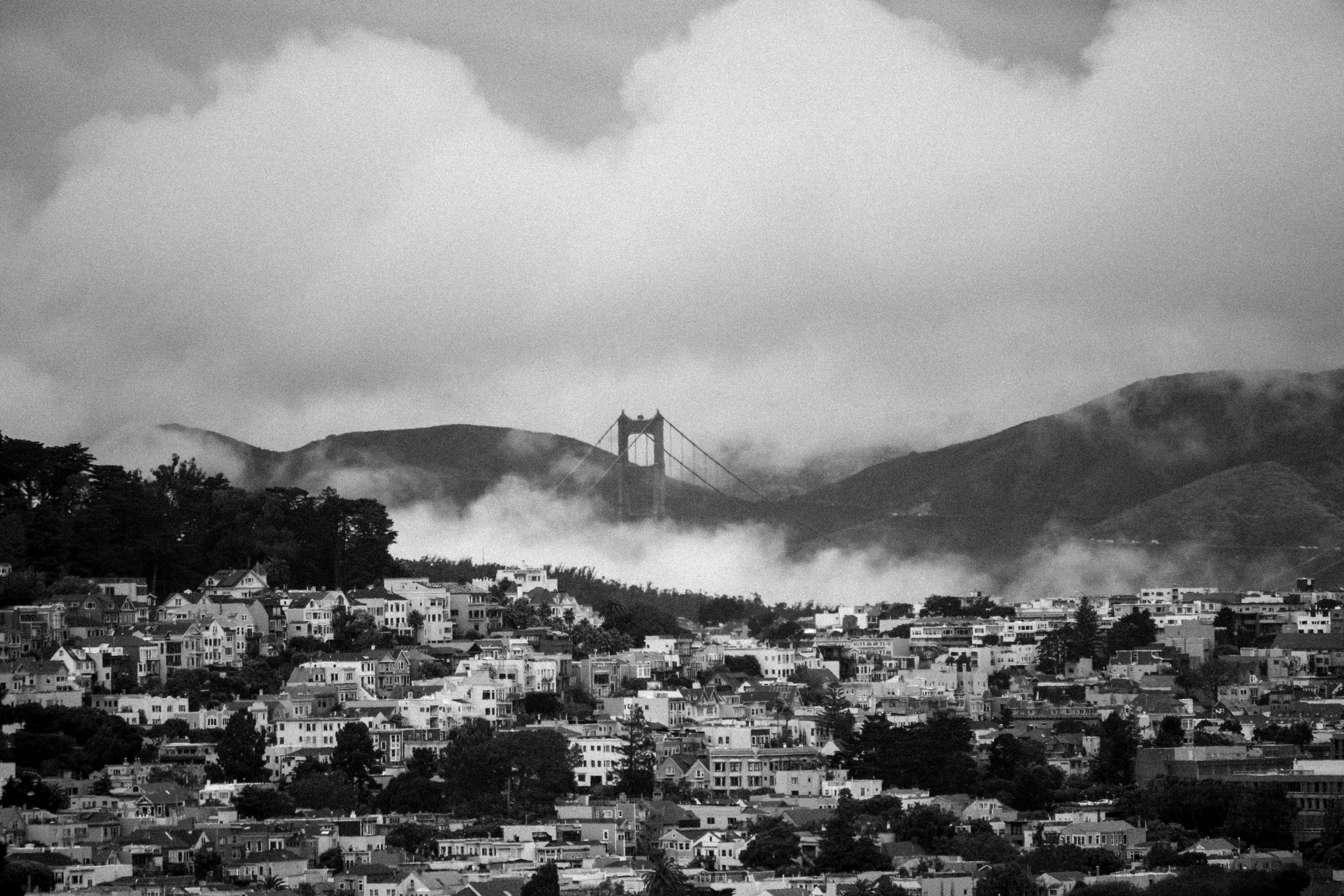 Black and white view of Golden Gate Bridge enveloped in fog above San Francisco cityscape.