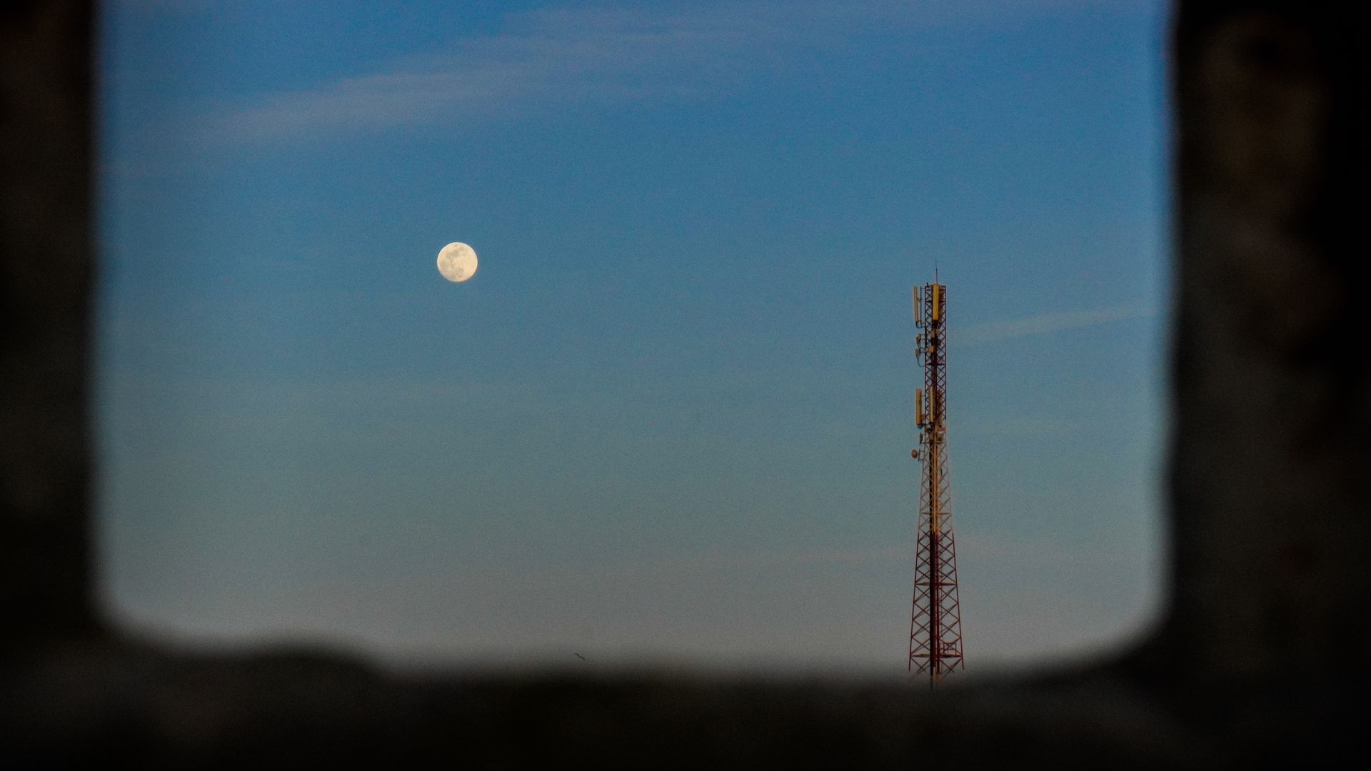 A serene evening scene featuring a moon and a communication tower against a clear sky.