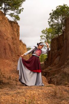 Woman in traditional dress performing a dance in a scenic canyon landscape.