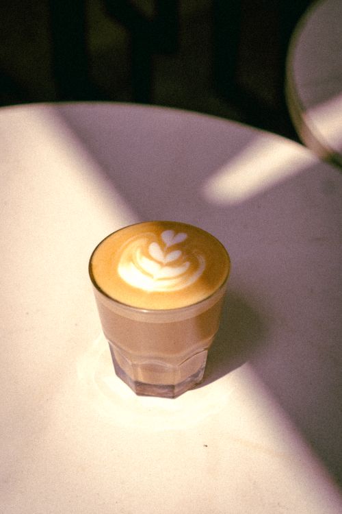 Free A beautifully crafted latte with intricate latte art served in a glass, illuminated by sunlight Stock Photo