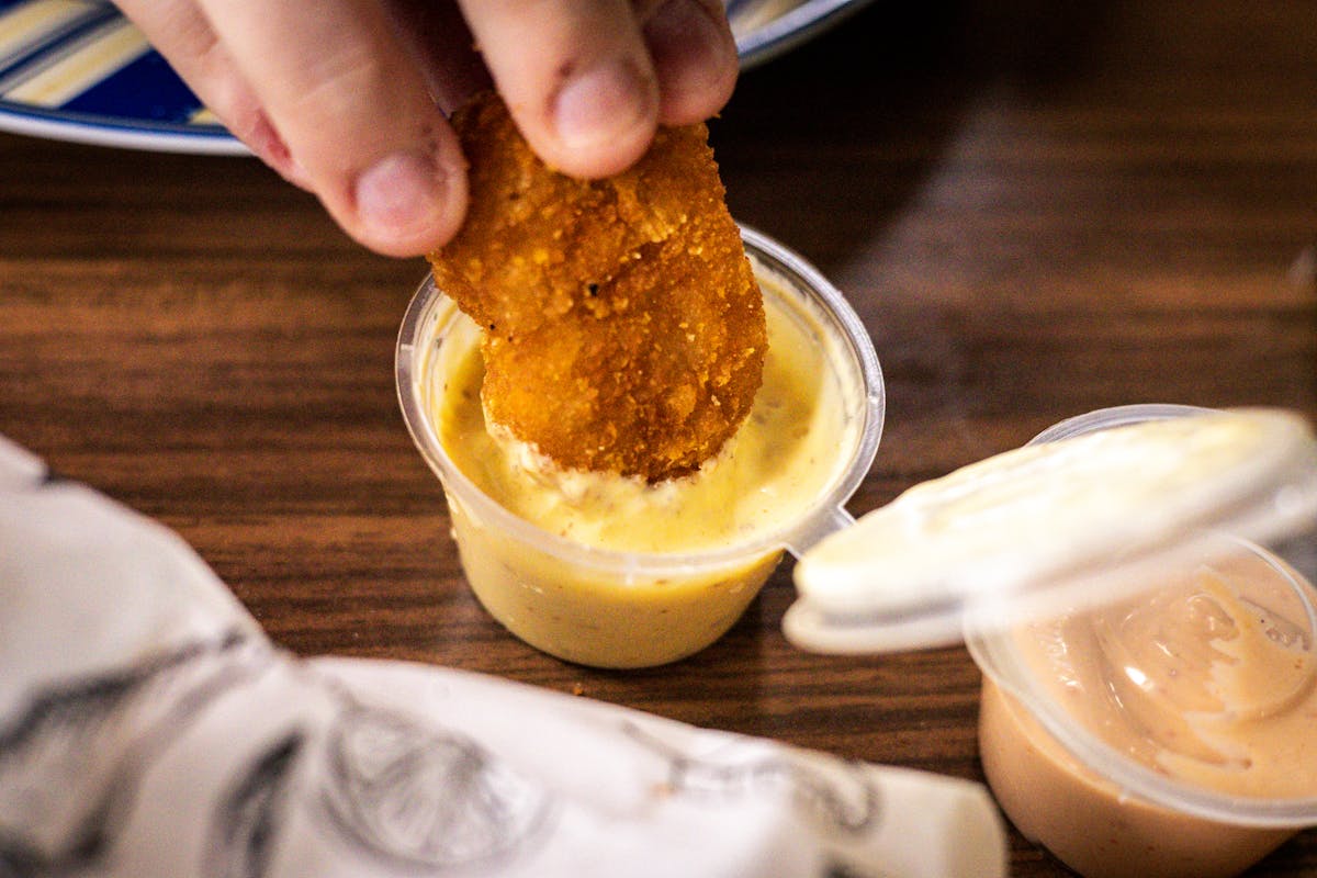 Crispy nugget being dipped into creamy yellow sauce