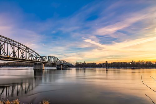 Free Beautiful sunset view of a steel bridge over calm river waters with a colorful sky. Stock Photo