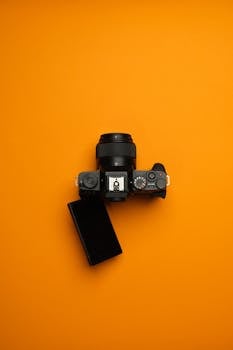 Top view of a modern mirrorless camera with adjustable screen on orange backdrop. Perfect for creative projects.