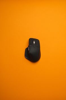 Modern black ergonomic mouse isolated on a striking orange background.