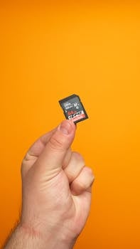 A hand holding a 64GB SanDisk SD card on a bright orange background, ideal for tech and photography themes.