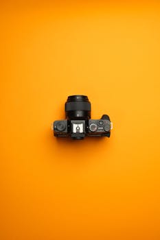 Flat lay of a sleek mirrorless camera on a vibrant orange background, showcasing modern photography gear.