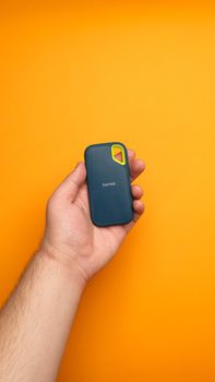 A hand holds a SanDisk portable SSD against a vibrant orange backdrop.