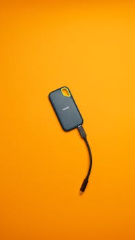 Portable SSD with USB-C cable on a bright orange background, perfect for modern tech enthusiasts.