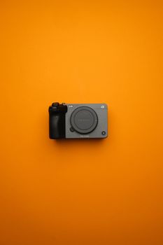 A sleek mirrorless camera displayed against a bold orange backdrop, emphasizing modern design.