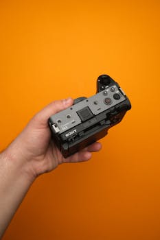 A sleek, handheld digital camera on an orange background, embodying modern technology.