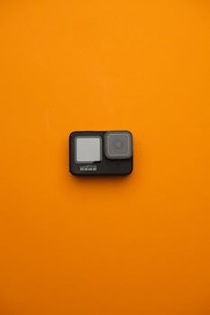 A sleek action camera displayed on a vibrant orange backdrop, emphasizing modern photography gear.