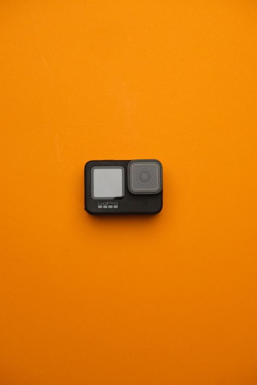Free A sleek action camera displayed on a vibrant orange backdrop, emphasizing modern photography gear. Stock Photo