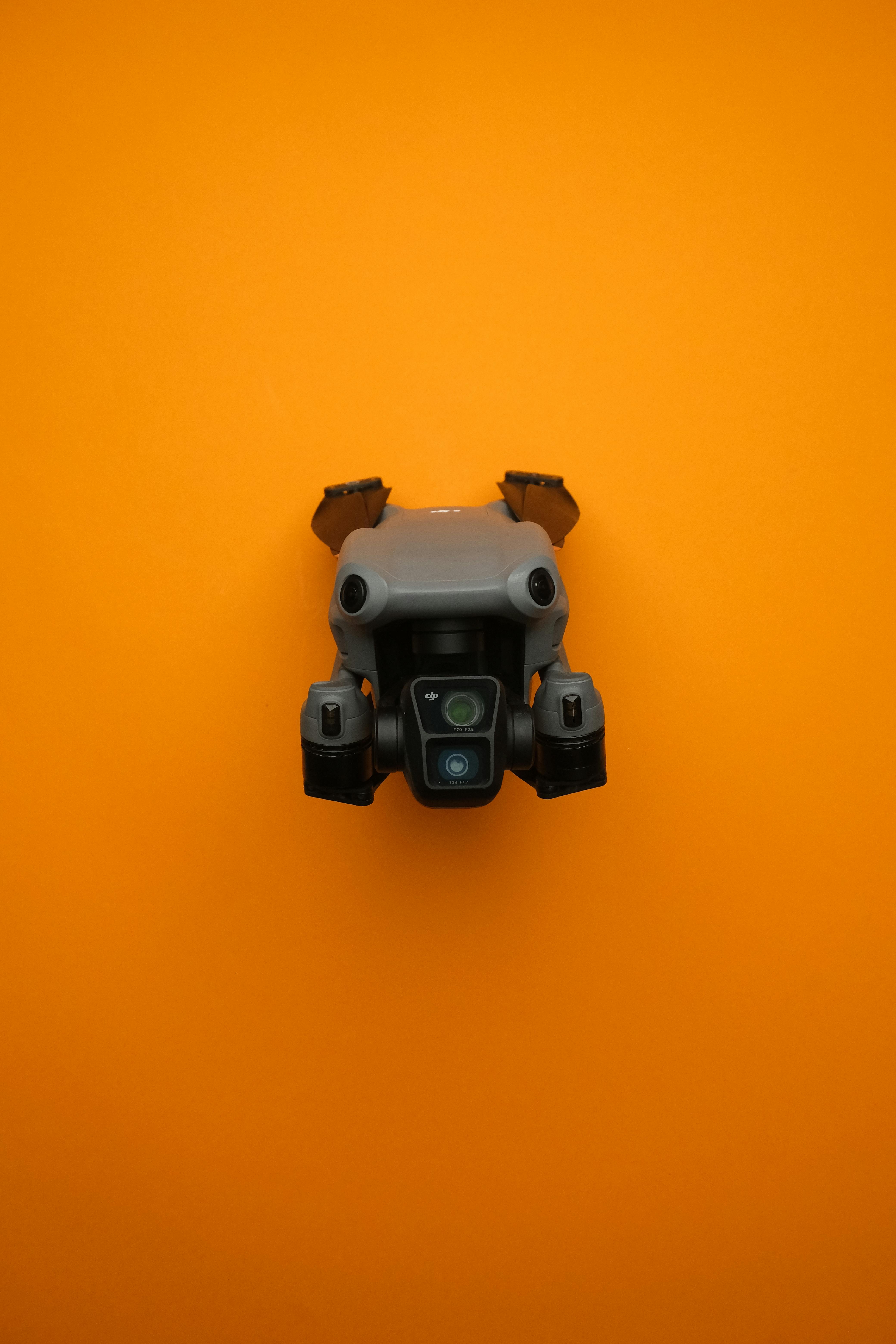 Close-up of a modern compact drone against a bright orange background, showcasing drone technology.