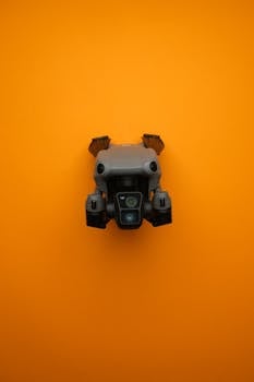 Close-up of a modern compact drone against a bright orange background, showcasing drone technology.