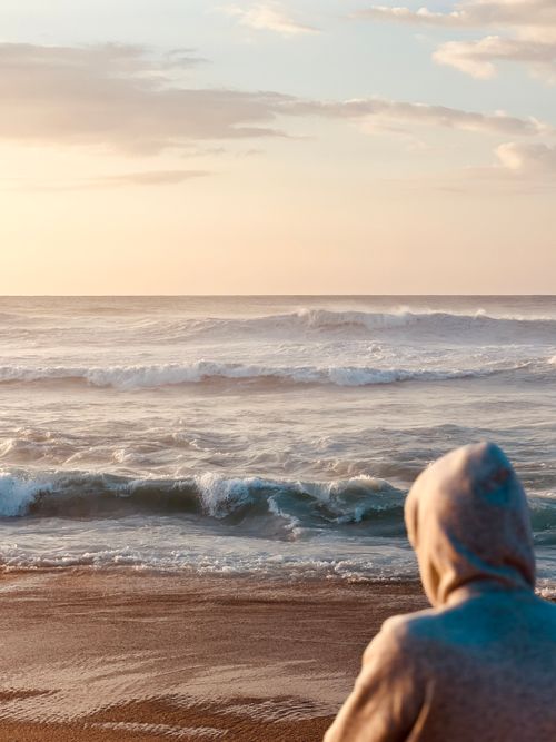 Free A person in a hoodie observes the waves at sunset on a Moroccan beach. Stock Photo