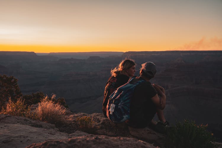 Man And Woman Sitting On Mountain Edge