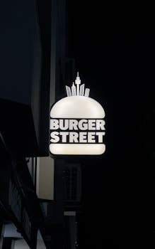 Neon Burger Street sign glowing against a dark night sky, featuring cityscape elements.