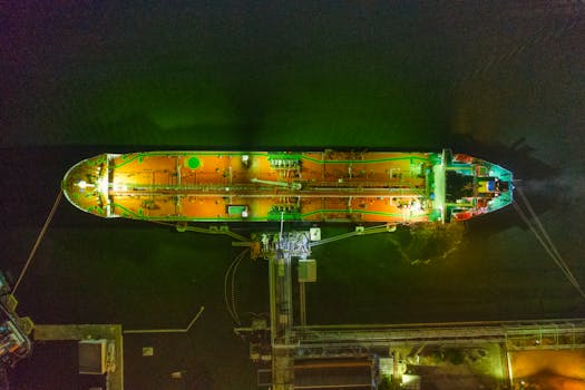 An aerial shot of a cargo ship docked at a pier in Jakarta, glowing under night lights.