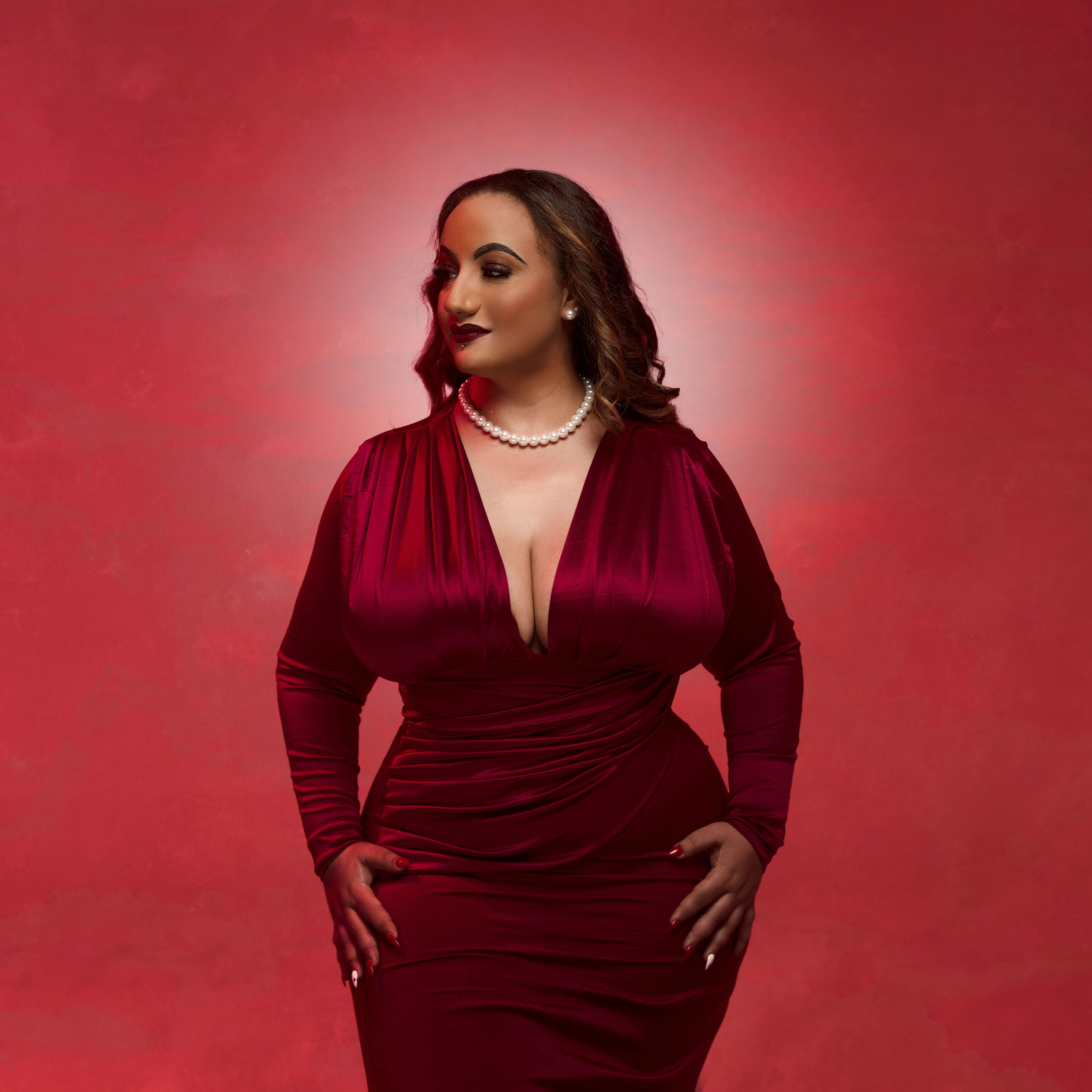 Portrait of a confident woman in a red dress and pearls on a red background.