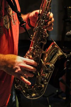 Detailed close-up of a musician playing an alto saxophone indoors, capturing the hands and instrument.