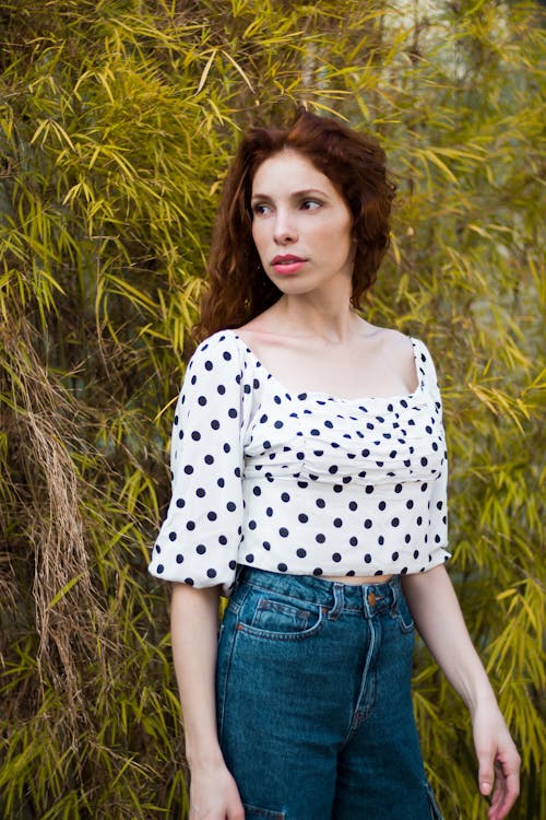 Photo of Woman in Polka-dot Top and Blue Jeans Posing While Looking Away