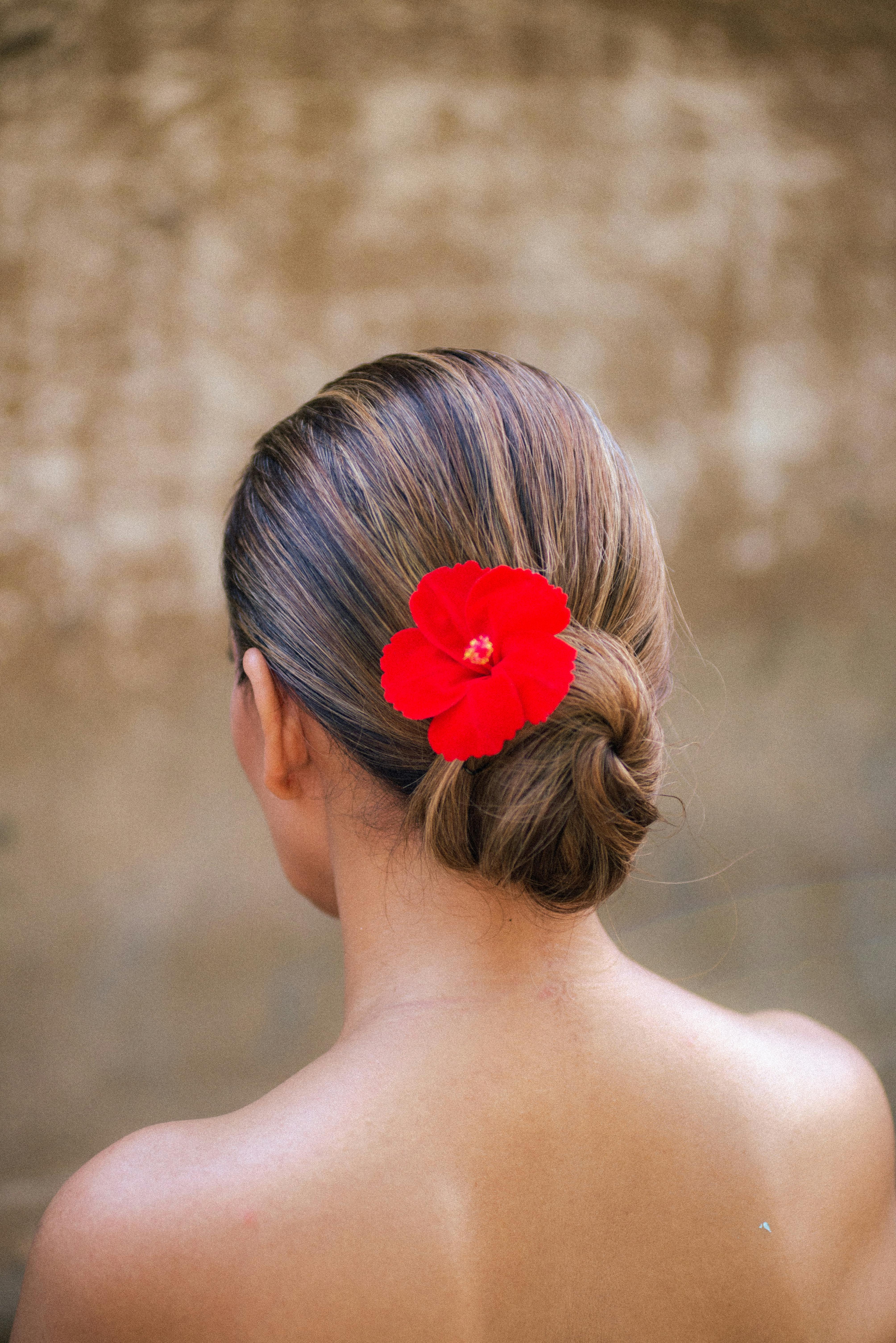 Back view of a woman with a red hibiscus flower adorning her hair in Bali, Indonesia.