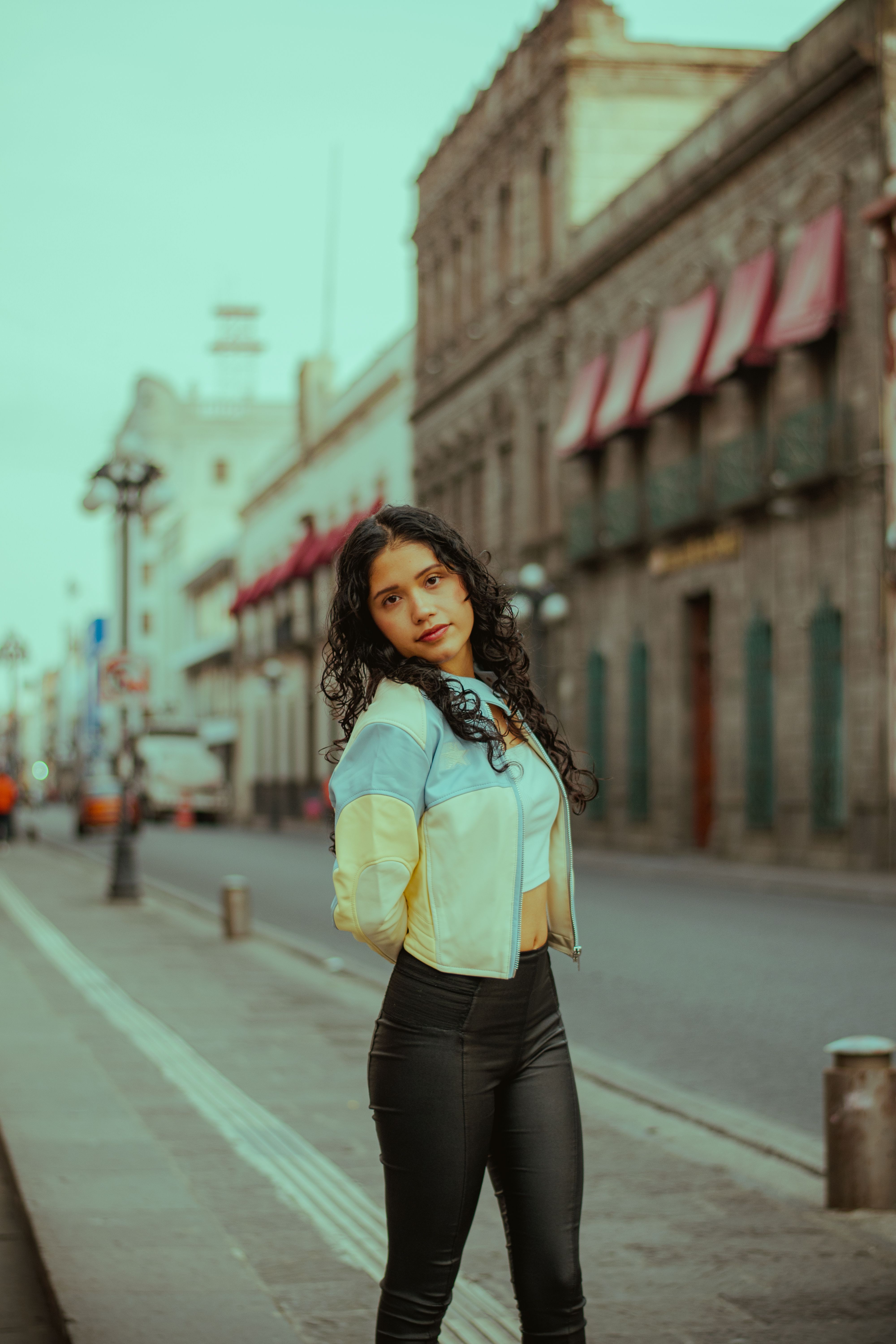 Young woman in urban setting, wearing fashionable attire, posing confidently.
